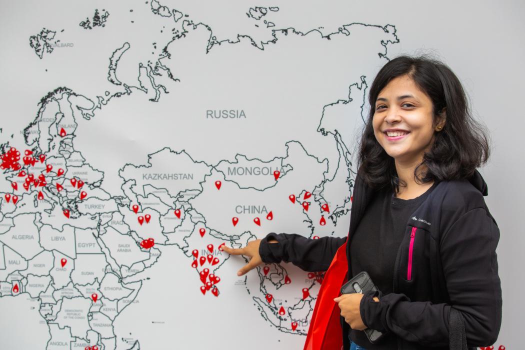 Student in front of a map covered in red stickers over various locations, pointing to India.